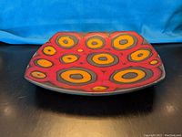Top-down view of the pottery dish showing vibrant concentric circle pattern in red, yellow, and orange.