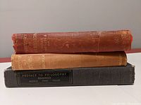 Stacked side view of three vintage hardcover books showing spines with titles and worn cloth bindings.