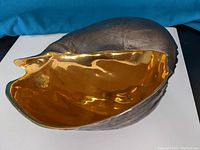 Top view showing shiny gold interior and dark textured exterior of seashell porcelain sculpture.