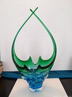 Front view of chalice-shaped art glass sculpture showing tall, open form with smooth green to blue gradient glass and clear bubble accents at the base.