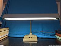 Front view of mid century airplane desk lamp highlighting wide lamp shade, base with red and black buttons, flexible copper goose neck, and power cord.