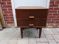 Front view of teak night table showing two drawers and tapered legs, with visible wear and marks.