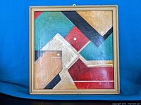Front view of the framed abstract geometric painting with red, green, beige, and black areas and white dots.