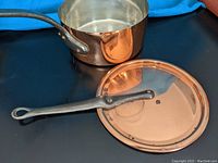 Photo showing copper pot with iron handle and matching lid placed beside it