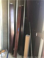 Four wooden bed rails in various brown tones, each with attached metal brackets, arranged vertically against a wall. Visible scratches on wood surfaces.