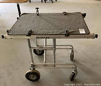 Side view of the Biosound adjustable cart showing the metallic frame, flat platform with six securing clips, and four wheels.