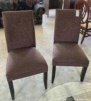 Both upholstered brown side chairs with wooden legs, showing general condition and one with a hole in the back upholstery