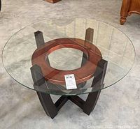 Full view of the round coffee table showing the beveled glass top and the wooden base structure.