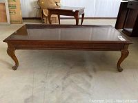 Full view of a rectangular wooden coffee table with carved legs and polished dark brown finish, placed on a concrete floor.