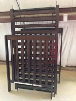 Dark wood crib frame parts including headboard, footboard, and side panels along with metal spring base, stacked and unassembled.