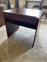 Front view of Palliser computer desk showing one drawer and dark brown laminate finish. Visible scratches and missing corner on right front edge.