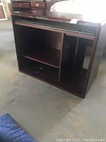 View of the front side showing the open shelving and slide out keyboard drawer, laminate peeling visible on front edges.