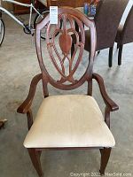 Front view of Bassett dining armchair with wooden carved back and cream padded seat.