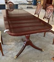 View of rectangular polished wood dining table with two chairs showing table surface and shape, including one of the two extension leaves attached.