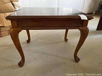 Front view of one wooden end table showing carved legs and decorative apron.