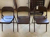 Three brown metal folding chairs arranged side by side, showing scratches and wear on seats.