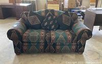 Front view of the love seat showing the rolled arms, patterned fabric, and pillows included.