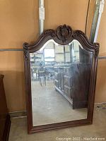 Full front view of beveled mirror with detailed wood frame and ornate carved top, showing overall item and condition.