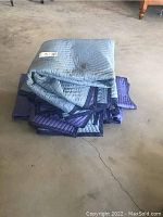 Stack of folded used moving blankets in various shades of blue and purple on concrete floor