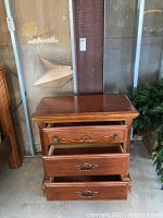 Night stand with three drawers open, carved wood details, metal handles shown, scratches visible on wood surface.
