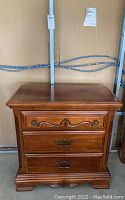 Front view of solid wood night stand showing three drawers, metal pulls, and decorative trim