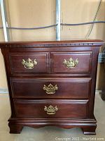 Front view of one wooden nightstand showing three drawers and brass handles, scratches visible