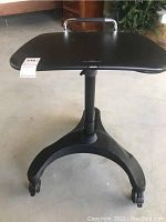 Front view of the Aidata rolling table showing black tabletop, central column, wide base with caster wheels and pull bar.