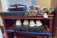 Overall lot showing 6 DCO exterior bullet cameras, 4 dome cameras, Night Owl DVR, VHS recorder and power adapters on wood stand.