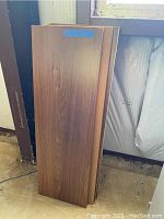 Four laminate shelves shown standing upright with a wood grain finish, some holes drilled, visible damage.