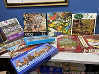 Grouped view of 8 of the puzzle boxes on a table showing titles and artwork including E.T., trains, Mosaic, teddy bears, Longwood Gardens, and Christmas tree.