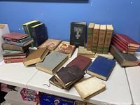 Books spread out on a table showing various titles, sizes, and conditions in a range of colored hardcovers including green, red, blue, and brown.