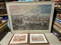 Photo of the three framed artworks including one large framed poster and two smaller framed prints laid on table.