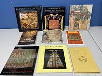 Nine books on Chinese clothing and textiles displayed on white table against blue background