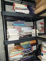 Books organized on black plastic shelving units, stacks of various titles in both hardcover and paperback form.