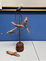 Full view of the folk art sculpture showing the wooden base, metal wire branches, and four birds attached with one bird placed on the table detached and broken.