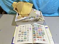 Photo showing the open stamp album with multiple pages of stamps and the box containing loose envelopes and stamps.