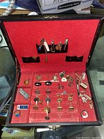 Open box showing cuff links and tie clips arranged on red velvet lining.