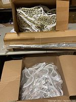 Box containing multiple white lacrosse heads, some strung, placed inside a cardboard box.