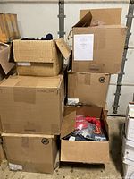 Eight large cardboard boxes stacked in a garage, each filled with assorted hoodies