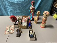 Photo showing entire lot of Japanese wood dolls, geisha doll, and various fabric dolls arranged on a table with blue backdrop.