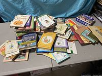 Large collection of children's books arranged loosely on a table, showing a variety of titles and subjects.