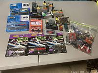 Full view of all items spread out on a table including boxed Matchbox sets, Johnny Lightning cars in packaging, Wheaties car, and a zip bag of loose cars.