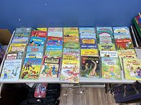 Top view of a table covered with many Little Golden Books including Disney, Sesame Street, Barbie and more children's titles, showing colorful illustrated covers and various story themes.