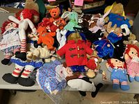 Full overview of lot showing Raggedy Anne dolls, Paddington bears, and various Beanie Babies on a table