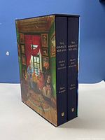Side view of the two hardcover books in decorative slipcase with illustrated room scene artwork.