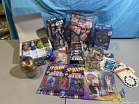Overview photo of the assortment of toys and collectibles listed in the lot, showing unopened packaging, boxed items and loose pieces.