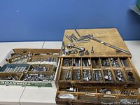 Photo showing the wooden divider box with multiple compartments holding various wrench sockets and socket accessories, some hinged sockets, and several T-handle extensions laid on top