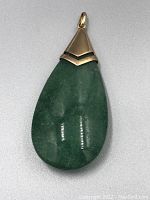 Front view showing the full teardrop-shaped green jade pendant with gold mounting and bail.