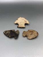 Top view of three vintage arrowheads showing their shapes and colors on a gray background.