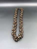 Cluster pearl strand necklace laid flat showing chocolate and beige colored pearls assembled closely with a silver clasp at top.